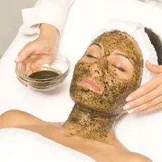 A herbal green peel mask being applied to a client resting on a treatment bed