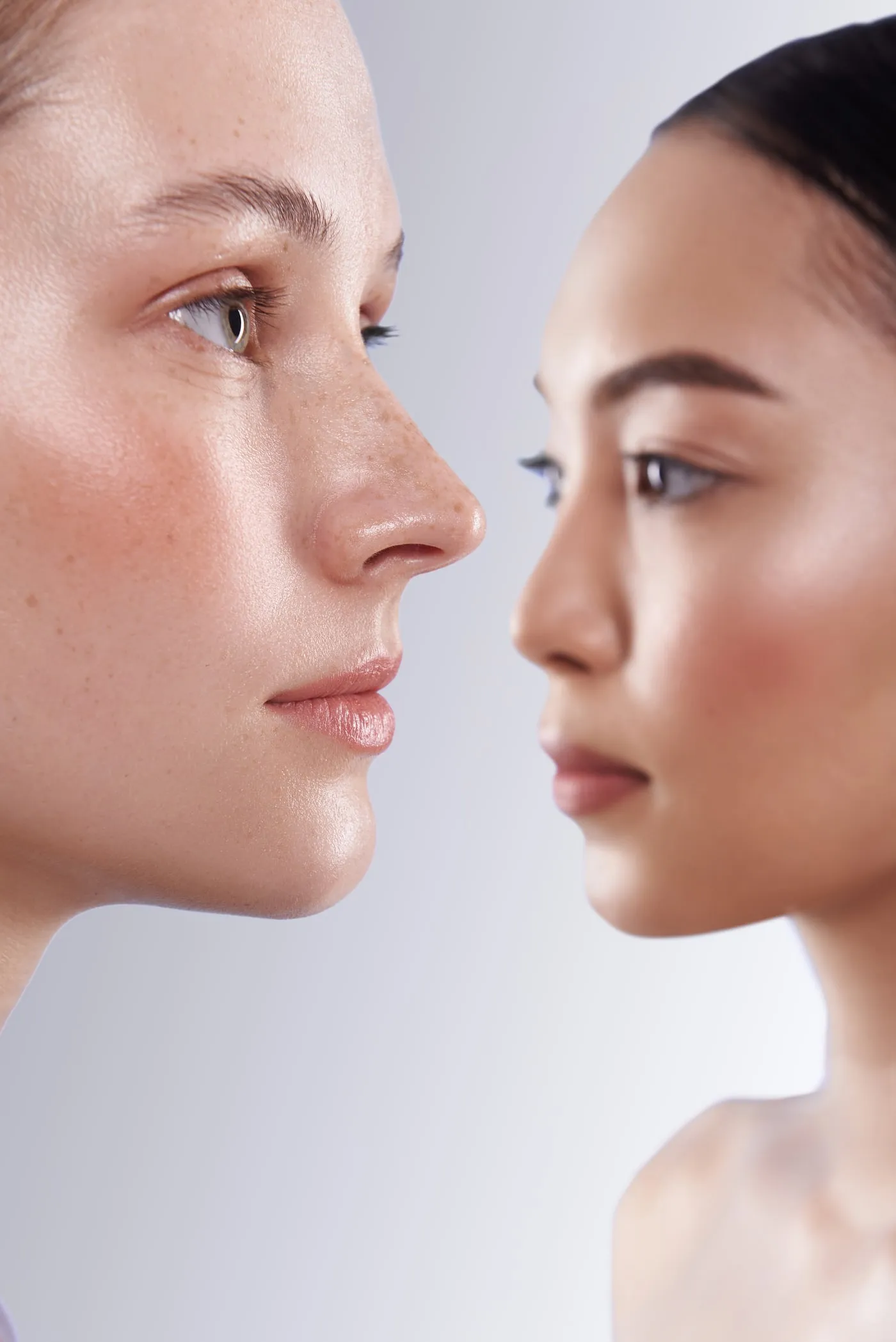 Two women in profile facing each other, both with clear, even skin